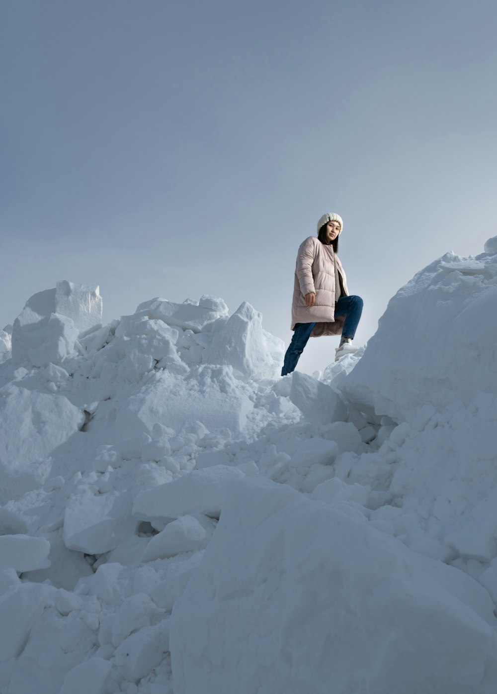 白いジャケットとブルーデニムのジーンズを着た女性が、昼間、白い雪に覆われた地面に立つ