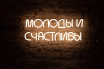White neon sign displaying Russian text against a textured, dark brick wall.