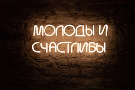 White neon sign displaying Russian text against a textured, dark brick wall.