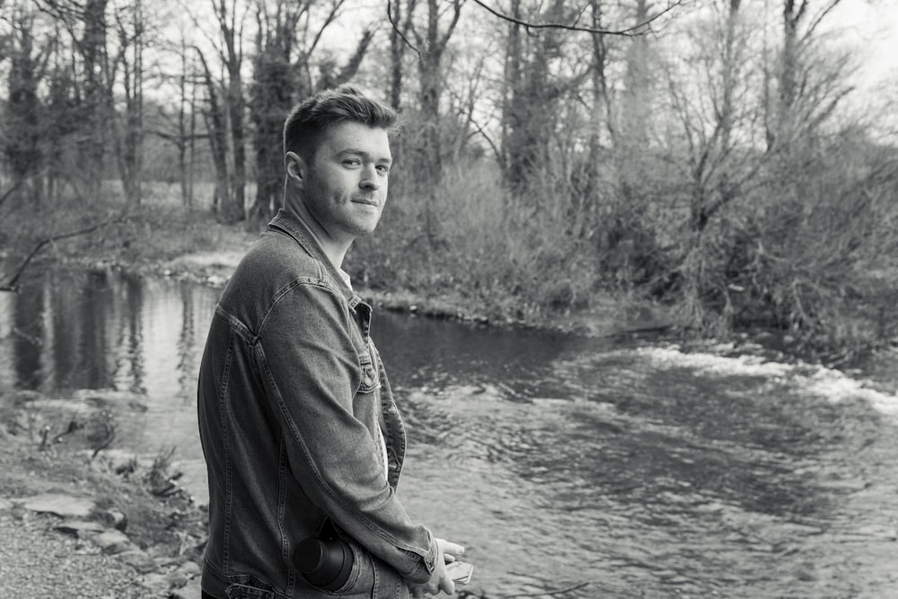 man in black jacket sitting on rock near river