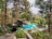 A swimming pool surrounded by lush greenery and trees, featuring a thatched-roof structure by the poolside. The area is peaceful and serene, suggesting a tropical or resort-like setting.