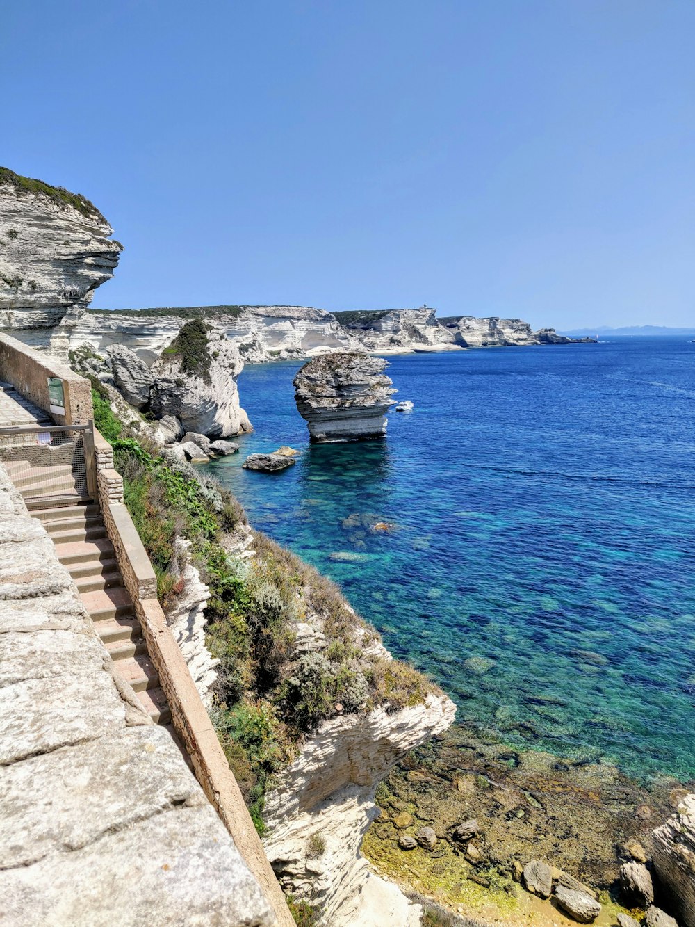 brown concrete stairs on gray rocky mountain near blue sea under blue sky during daytime