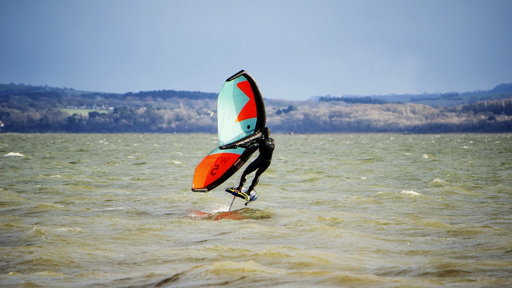 man in black wet suit riding orange kayak on sea during daytime