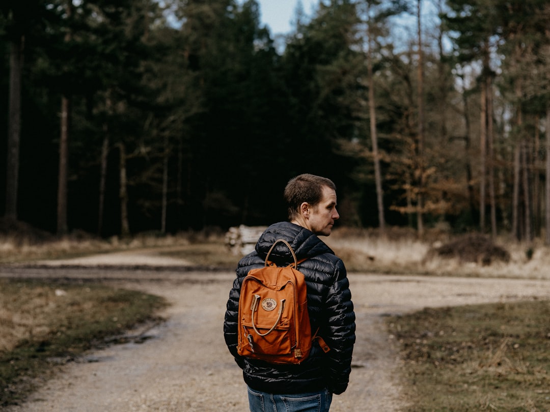 man in black and orange jacket walking on dirt road during daytime