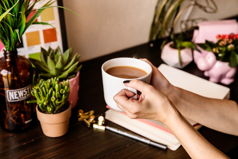 Persona sosteniendo una taza de cerámica blanca en la página blanca del libro