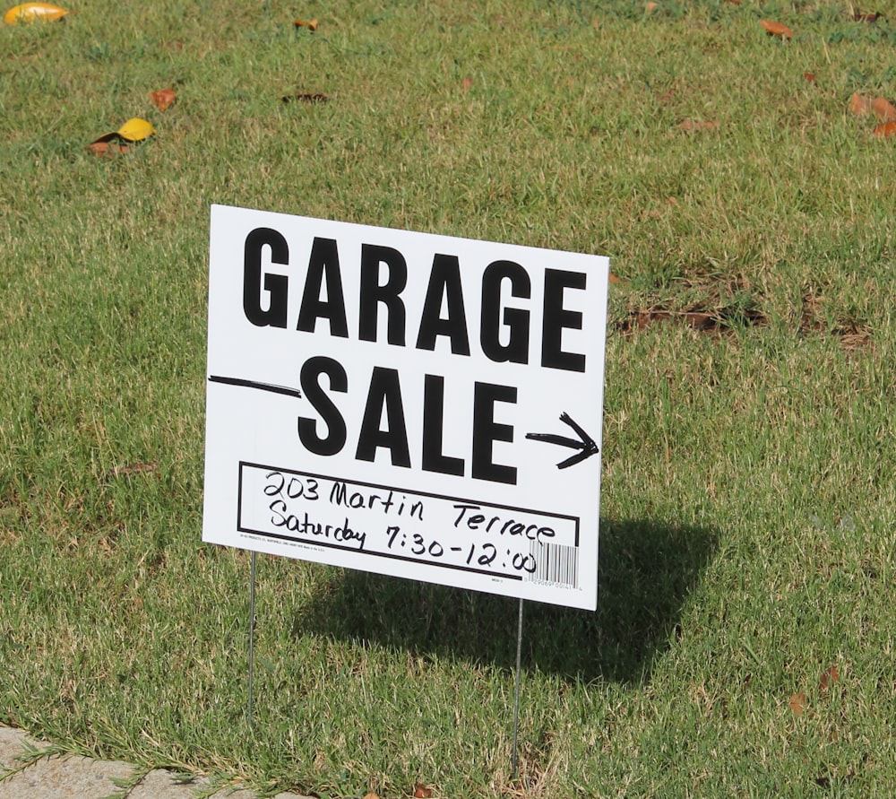 a white garage sale sign sitting in the grass