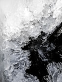 Cluster of translucent and crystalline ice formations, resembling natural ice sculptures, enveloping a darker void at the center. Textures appear smooth yet irregular, capturing the refraction of light within the ice.
