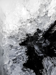Cluster of translucent and crystalline ice formations, resembling natural ice sculptures, enveloping a darker void at the center. Textures appear smooth yet irregular, capturing the refraction of light within the ice.