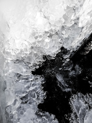 Cluster of translucent and crystalline ice formations, resembling natural ice sculptures, enveloping a darker void at the center. Textures appear smooth yet irregular, capturing the refraction of light within the ice.