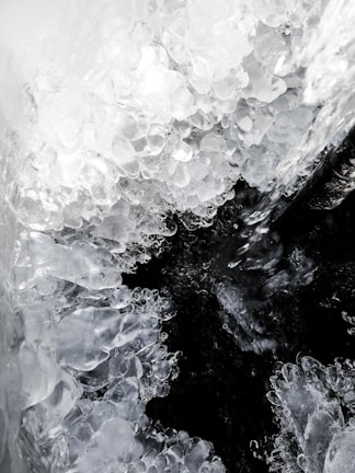 Cluster of translucent and crystalline ice formations, resembling natural ice sculptures, enveloping a darker void at the center. Textures appear smooth yet irregular, capturing the refraction of light within the ice.