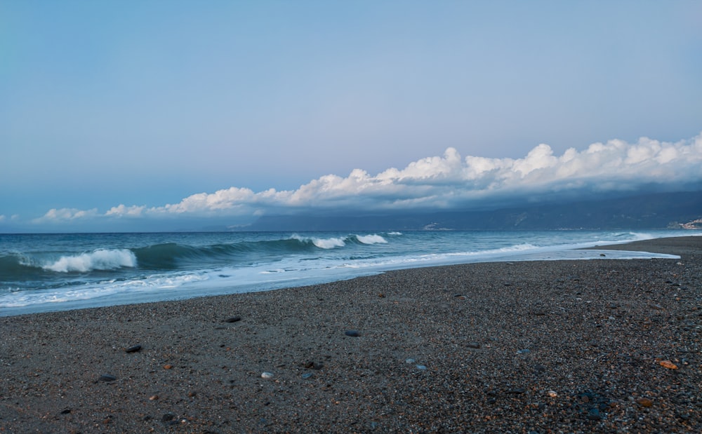 sea waves crashing on shore under white clouds during daytime