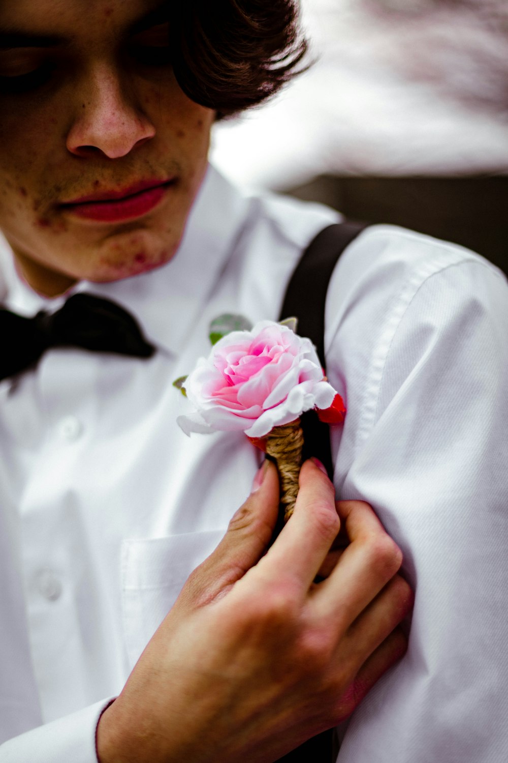 man in white dress shirt with black bowtie holding pink rose
