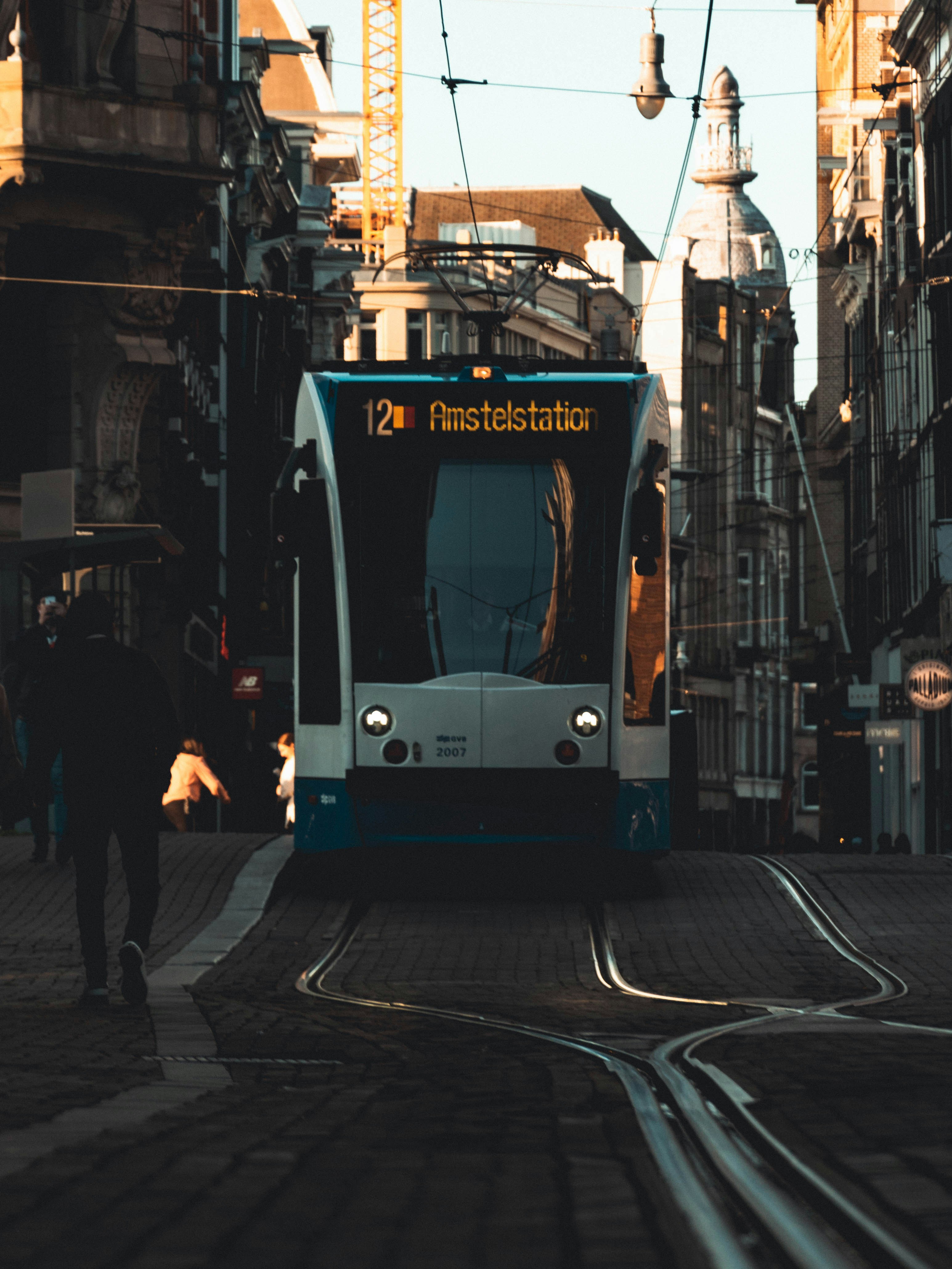 people walking on sidewalk near white and blue tram during daytime
