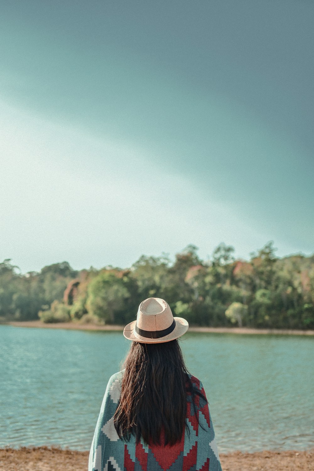 woman in blue and red plaid shirt wearing white fedora hat standing near body of water