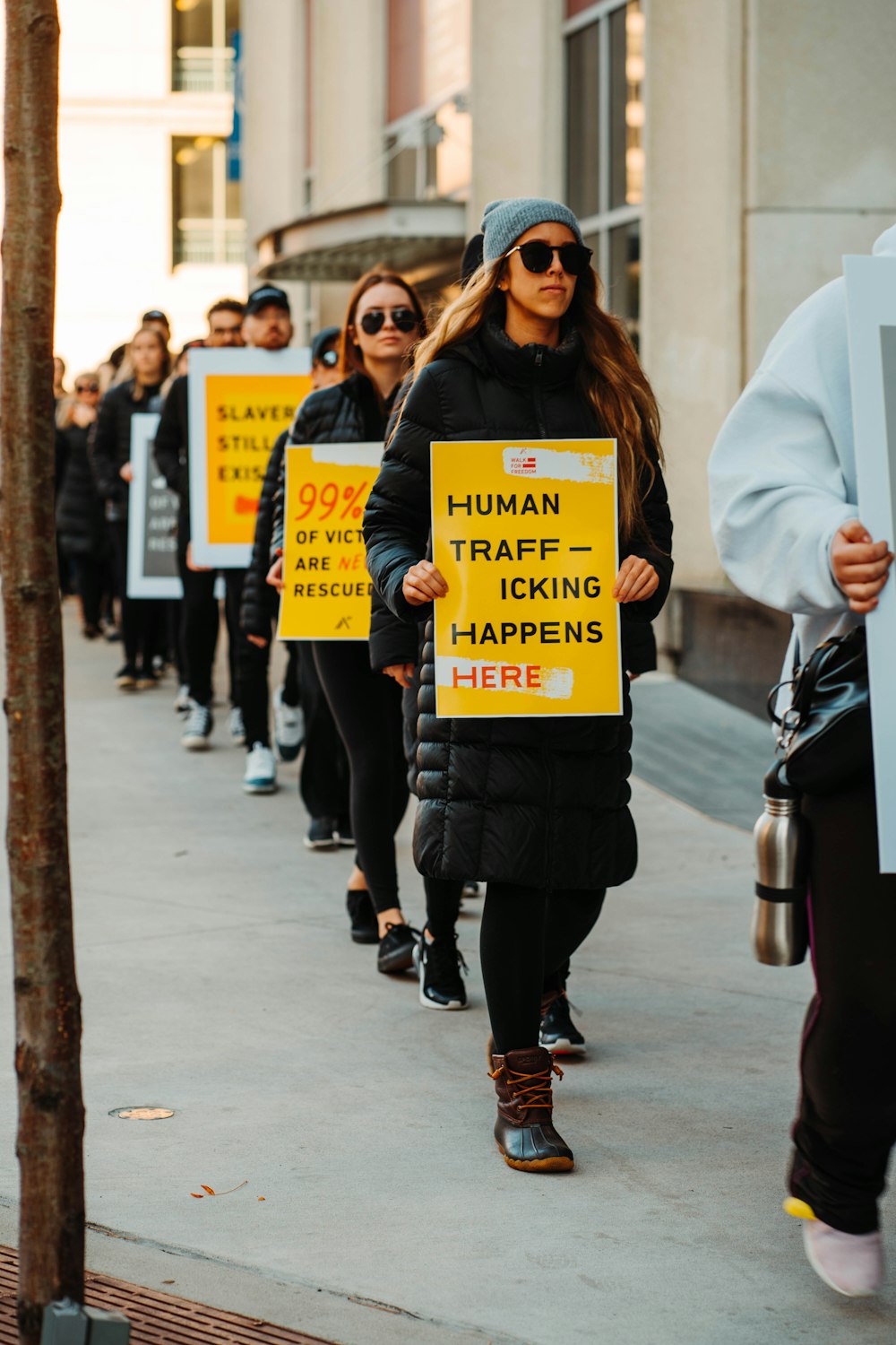 woman in white coat holding yellow and black signage