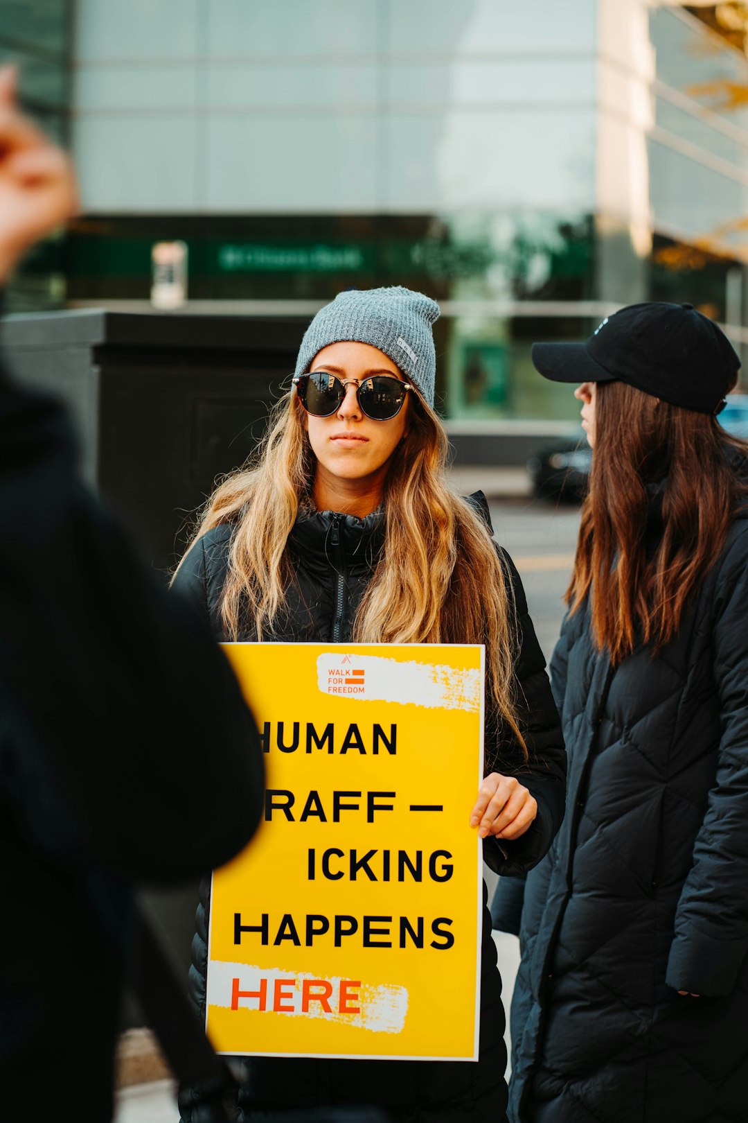 woman in black jacket wearing black sunglasses holding yellow and black signage