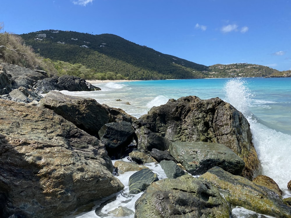 rocky shore with green mountain in distance under blue sky during daytime