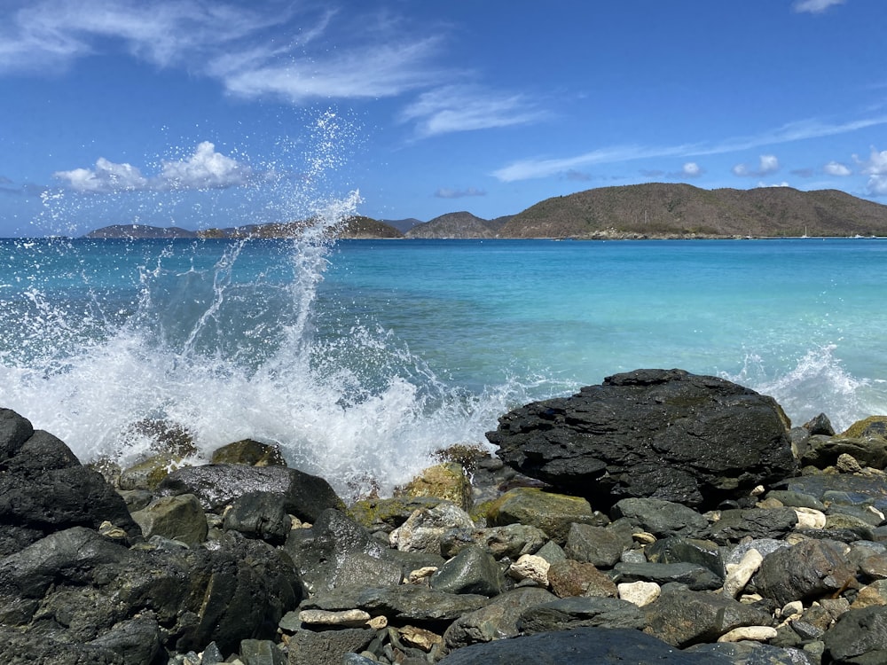 costa rocosa con olas del océano rompiendo en rocas bajo el cielo azul durante el día