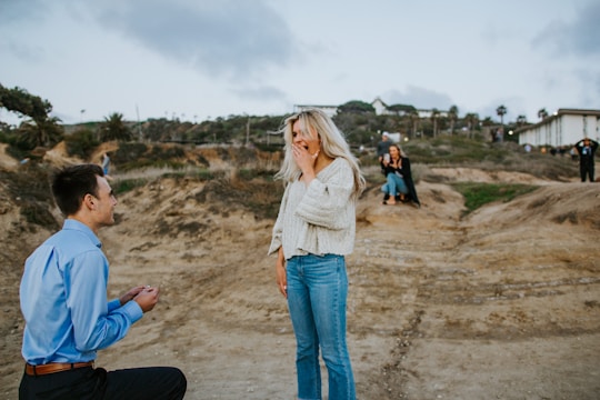 woman in white long sleeve shirt and blue denim jeans standing on brown sand during daytime