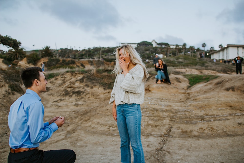 woman in white long sleeve shirt and blue denim jeans standing on brown sand during daytime