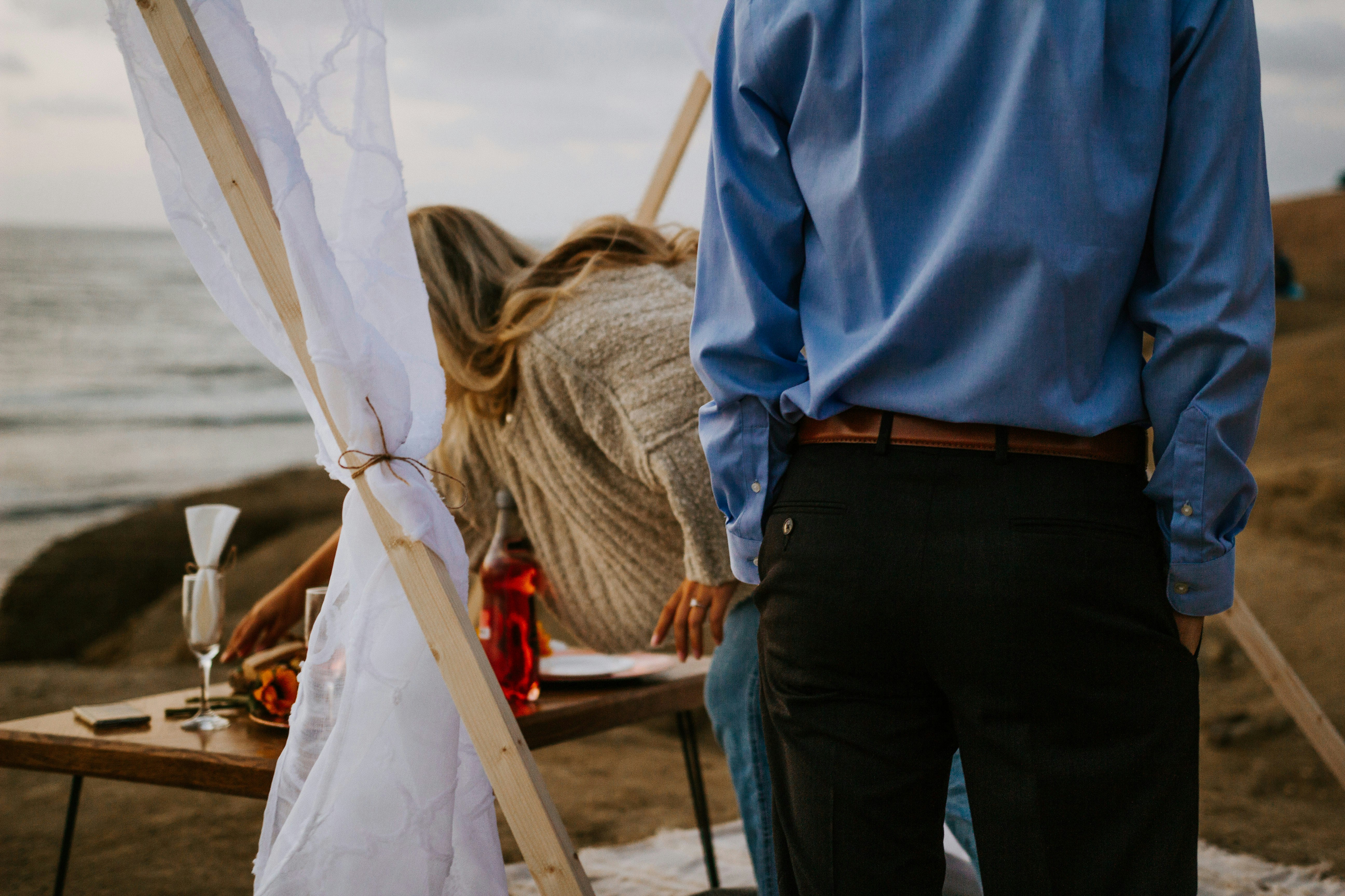 man in blue dress shirt and black pants standing near brown wooden table