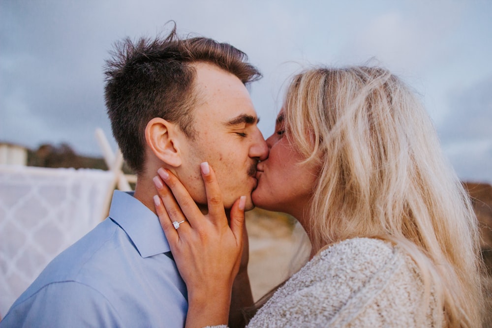 homem na camisa social azul beijando a mulher no suéter de malha branco