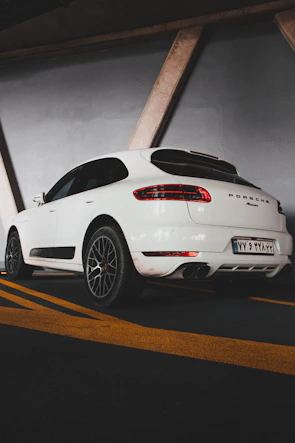 A Porsche Macan parked on a desert road flanked by rugged red rocks and cacti.