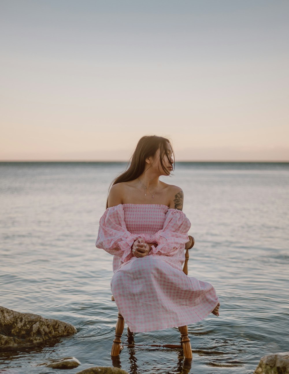 woman in pink and white floral off shoulder dress standing on rock near body of water