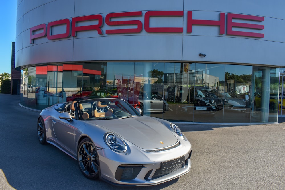 a silver porsche parked in front of a porsche dealership