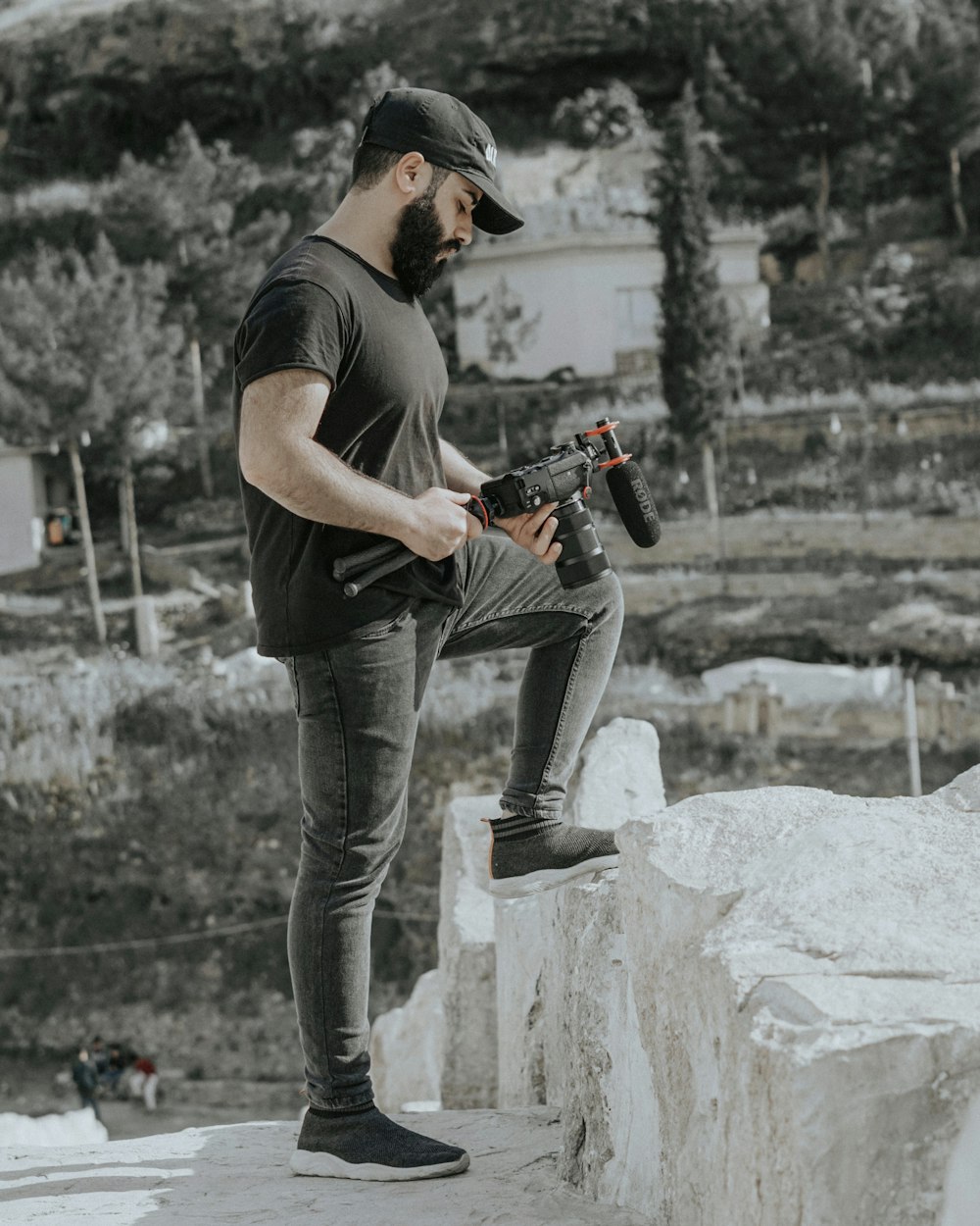 man in black t-shirt and blue denim jeans holding black and orange dslr camera