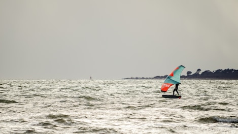 person in black wet suit riding red and black surfboard on sea during daytime