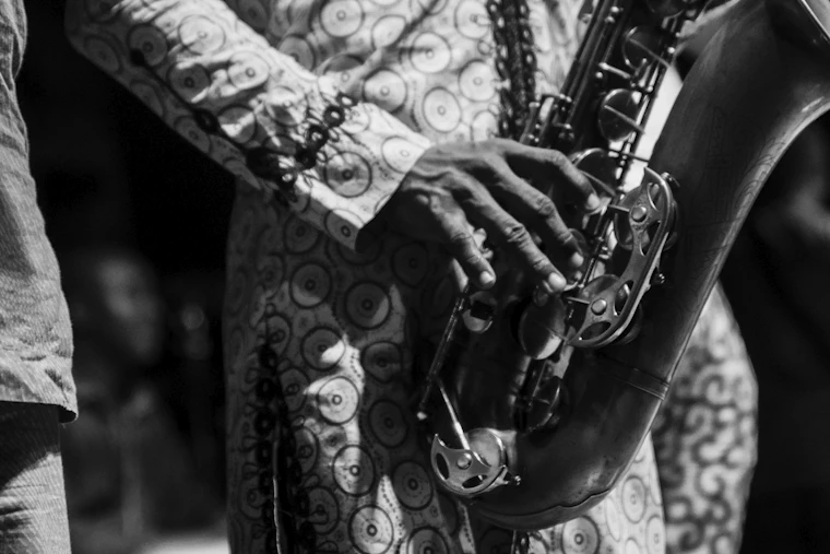 Mains d'un saxophoniste posées sur les clés de son instrument, manches d'une chemise à motifs, tirage noir et blanc.