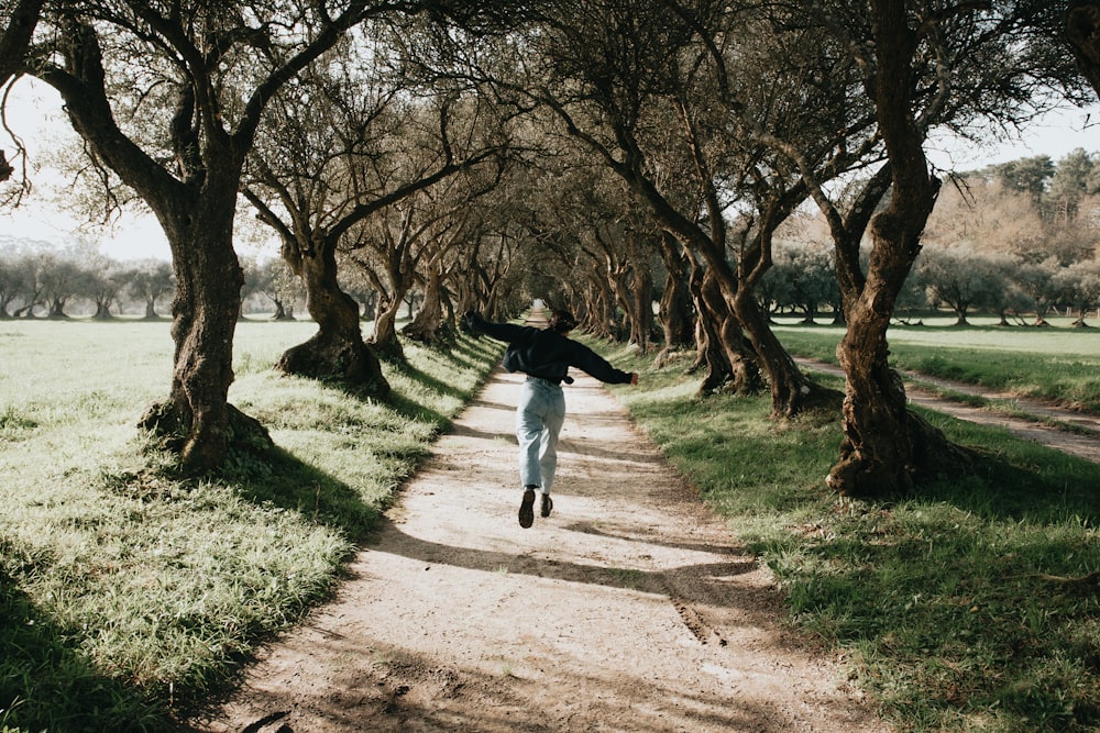 man in black jacket and white pants walking on brown dirt road during daytime