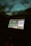 A car dashboard displaying a digital screen with music playing. The screen shows a song by an artist, with album art clearly visible. The surrounding dashboard is dimly lit, and the ambient light outside the car is low, giving a nighttime feel.