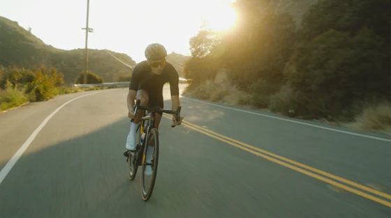 Ciclista de estrada pedalando rumo ao nascer do sol dourado