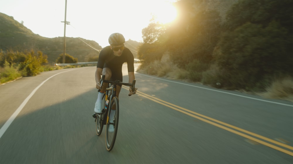hombre en camiseta negra montando en bicicleta en la carretera durante el día