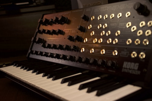 A moody close-up of a vintage synthesizer with glowing knobs under dim purple lighting.