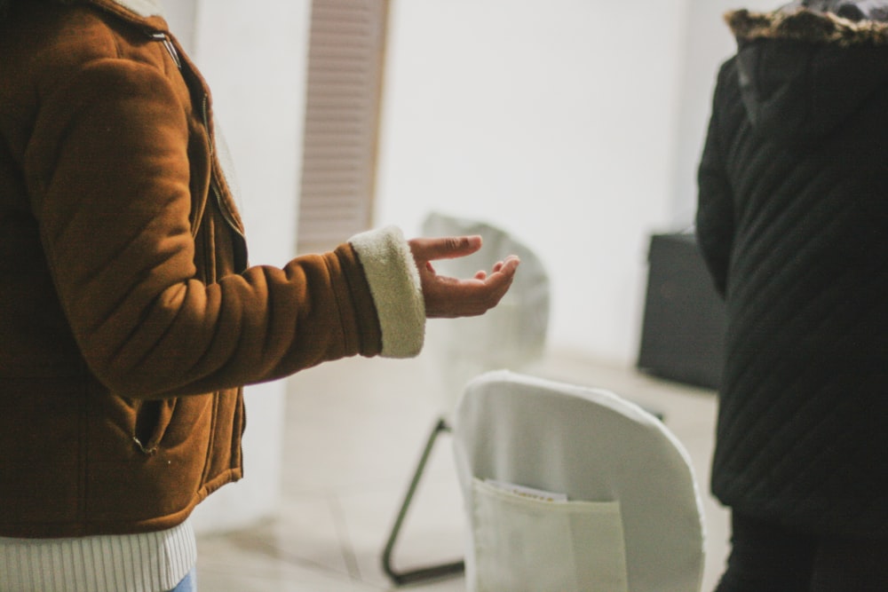 person in brown jacket holding white ceramic mug