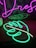 A vibrant neon sign with a green monstera leaf design is placed on a desk, alongside pink neon cursive text against a backdrop featuring a cityscape.