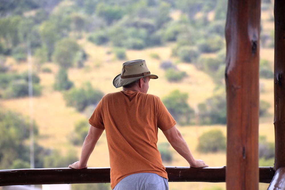 Hombre con camiseta naranja de cuello redondo y jeans de mezclilla azul sentado en un banco de madera marrón