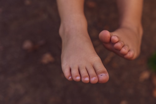 A pair of bare feet with clean toenails against a blurred earthy background.