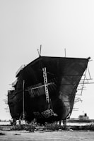 Steel ship docked, mid-fabrication with workers welding on the deck.