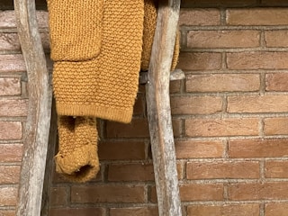 A handcrafted wooden blanket ladder leaning against a cozy, softly lit living room wall with a chunky knit throw draped over it.