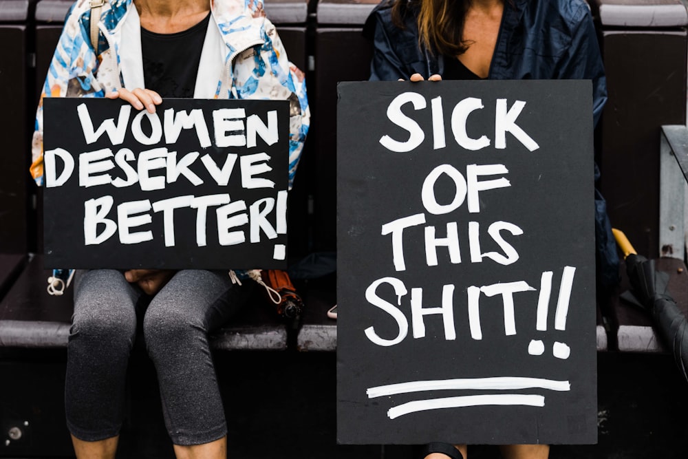 Ein paar Frauen sitzen nebeneinander und halten Schilder