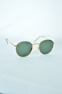 A pair of round sunglasses with green lenses and gold frames, positioned on a light-colored surface.