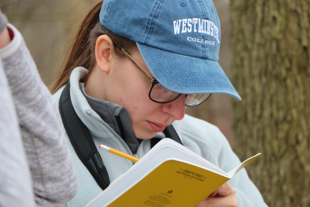 woman in blue knit cap and blue framed eyeglasses reading book