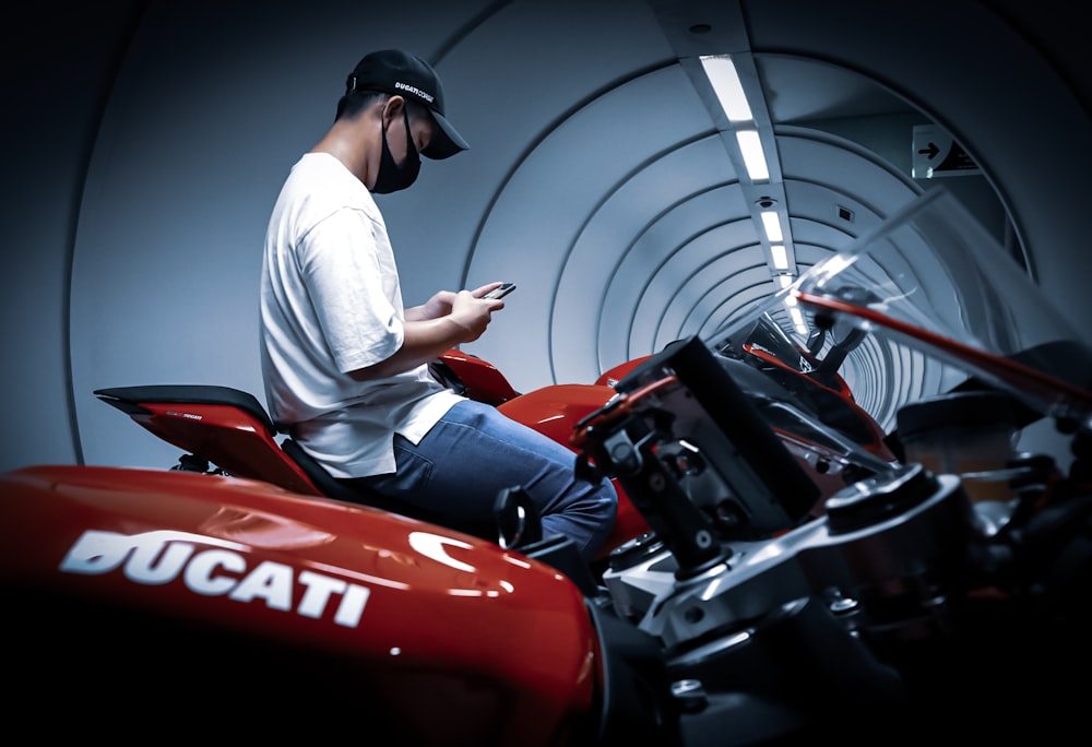 man in white t-shirt and black pants sitting on red and black sports car