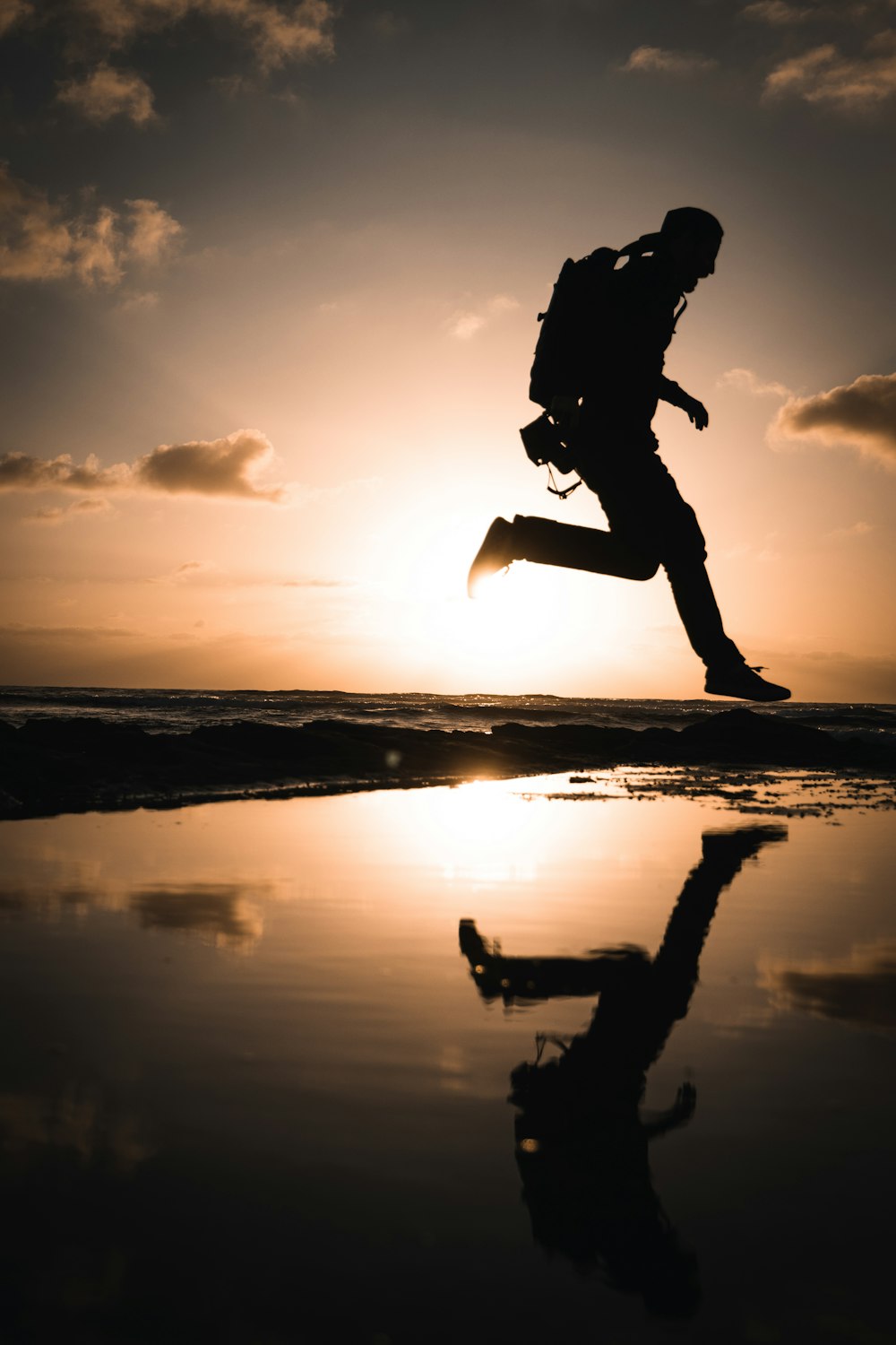 Silueta del hombre saltando sobre el agua durante la puesta del sol