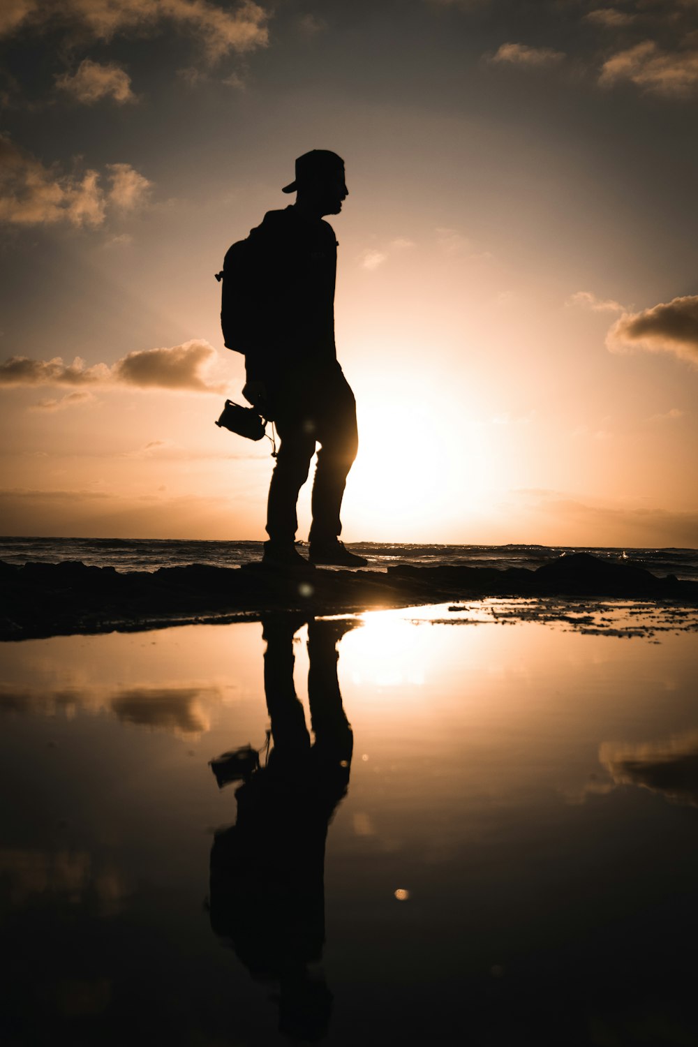 Silhouette einer Frau, die während des Sonnenuntergangs am Meeresufer steht