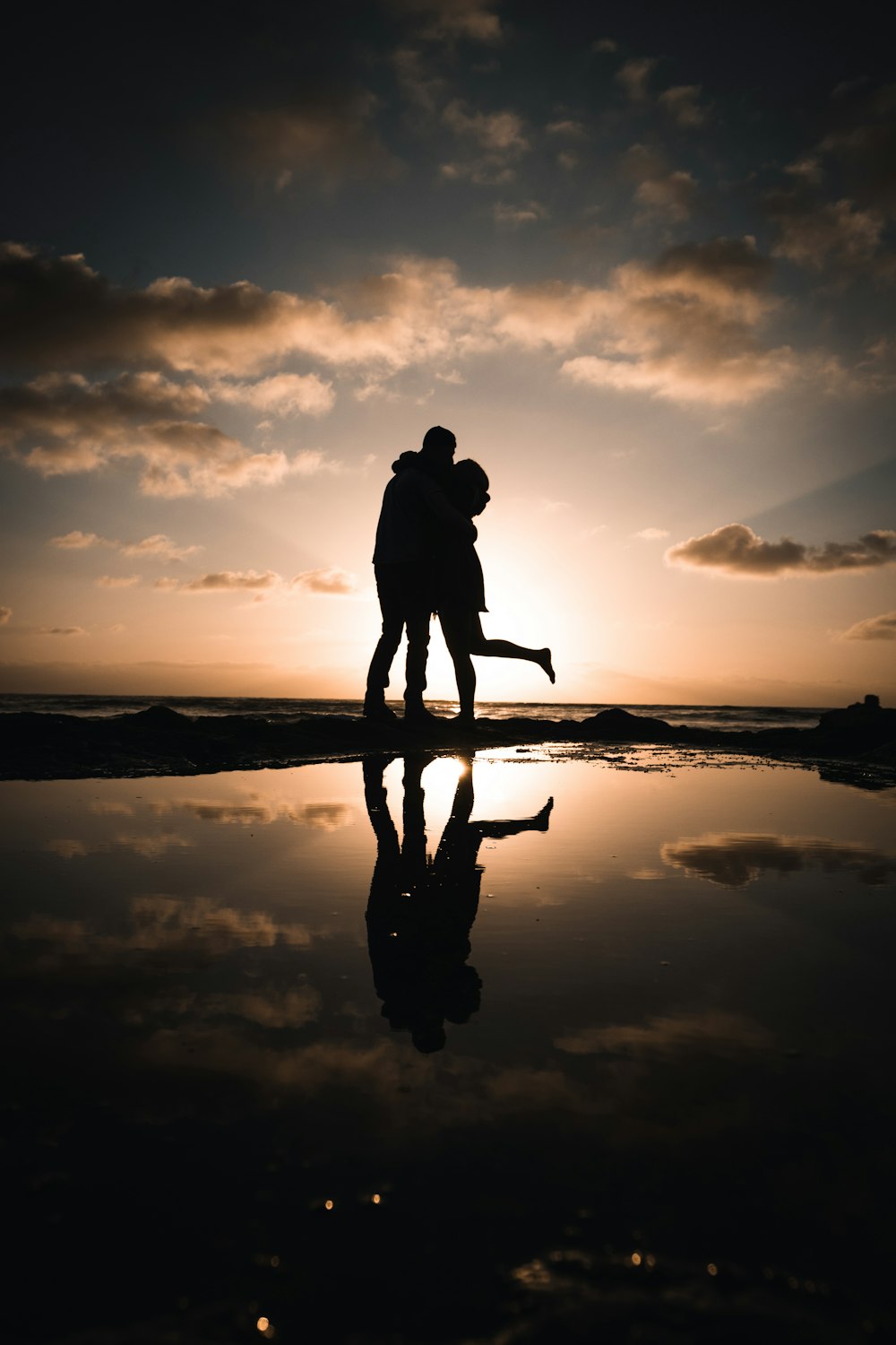 Silueta del hombre y de la mujer de pie en la orilla del mar durante la puesta del sol